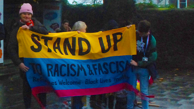 Banner says 'STAND UP TO RACISM AND FASCISM'