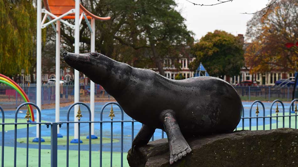 A bronze statue of a seal against a water park