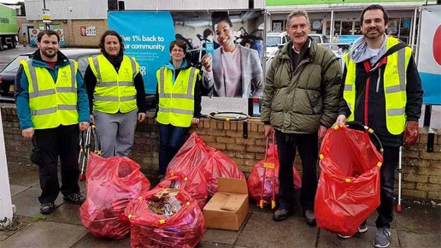 Five people, four in high-vis vests stand with trash bags