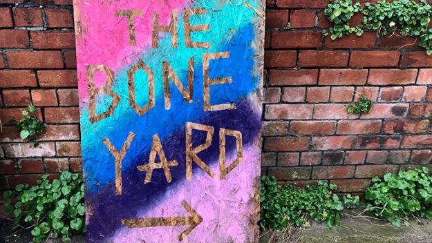 A pasteboard sign with the words 'The Bone Yard' painted against a rainbow background