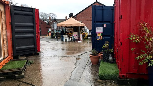 A courtyard surrounded by brightly painted shipping containers with a pop-up tent at the far end.