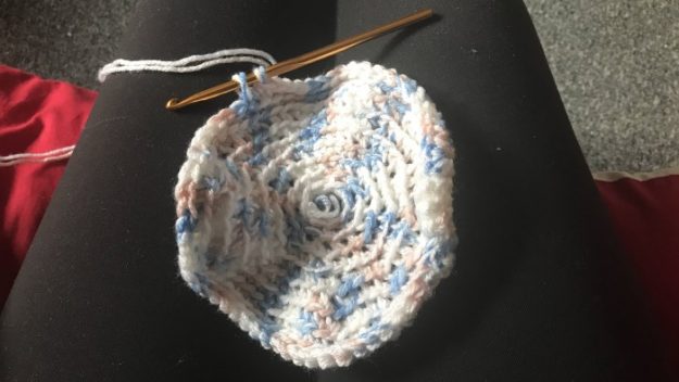 A circular potholder made with yarn sitting on someone's lap.