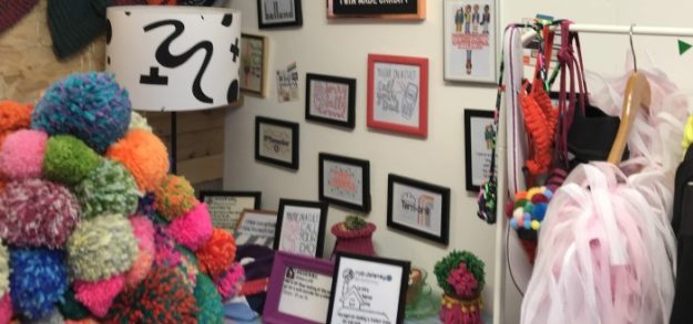 A shop interior fully of pompoms with framed embroidery pieces on the walls.