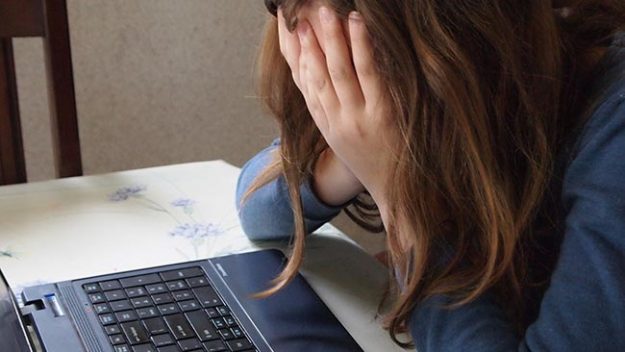 A young girl covers her head with her hands next to a computer