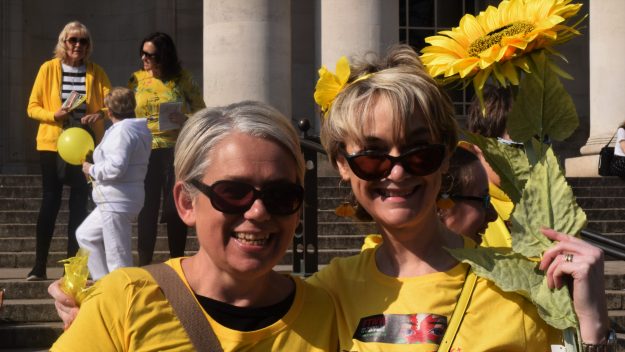 Two women wearing yellow shirts, one holding a sunflower, at the Cardiff EndoMarch 2019 to raise awareness for endometriosis