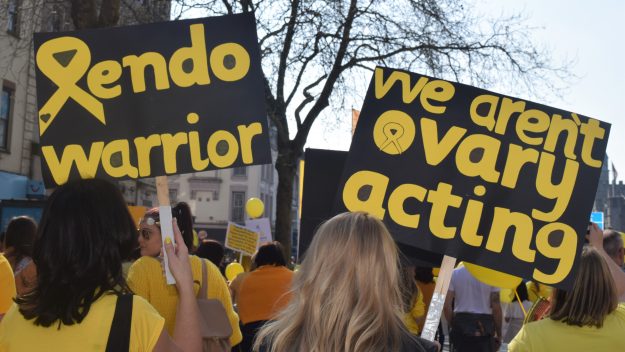 Two women carrying signs that read "endo warrior" and "we aren't overary-acting" to raise awareness for endometriosis at the EndoMarch 2019