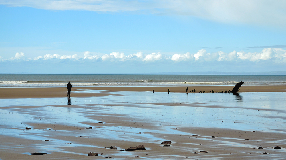 A beach with the silhouette of a man in the distance, a part of the communities along the Welsh coast.