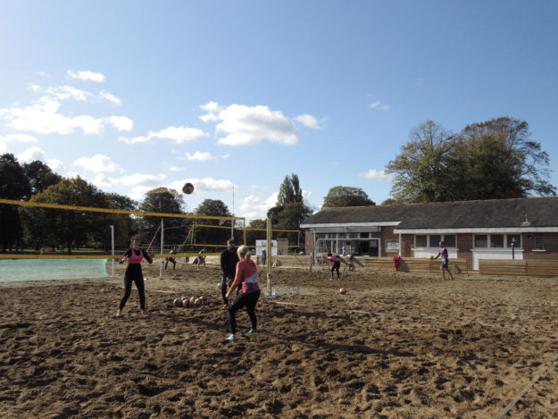 People are playing beach volleyball on large sand courts in the park.