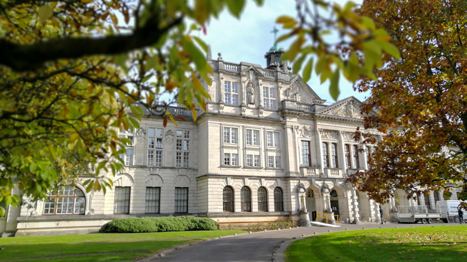 view of Cardiff University main building, seen through branches and framed by autumnal leaves. 