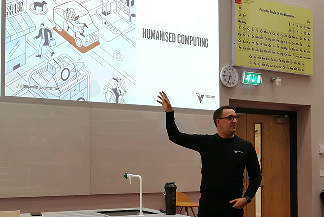 man giving presentation in lecture theatre gestures at projection screen