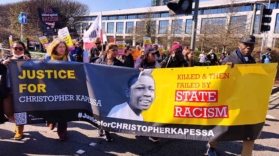 People holding up a banner with Christopher Kapessa's picture that says "Killed & Then Failed by State Racism