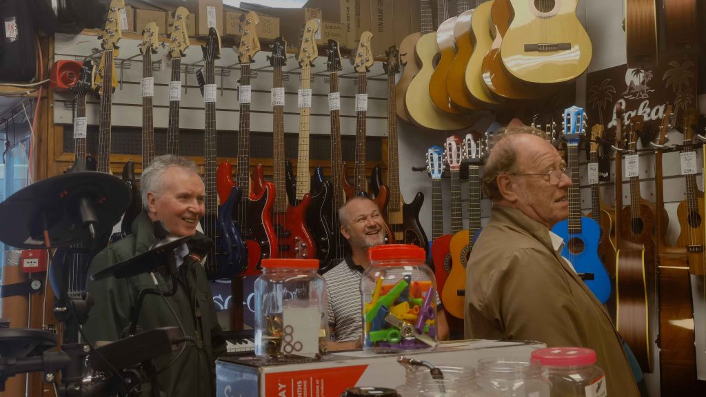 Two passing by old men in GM Music are considering to select a new guitar.