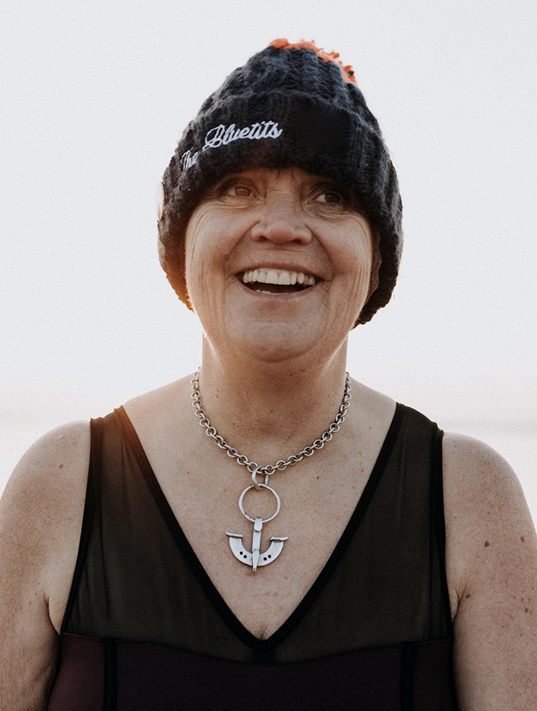 Sian Richardson, founder of cold-water swimming group, The Bluetits, stands smiling in her swimsuit and bobble hat