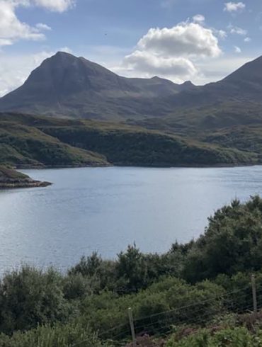 Mountains behind a loch in Scotland with greenery surrounding the shore