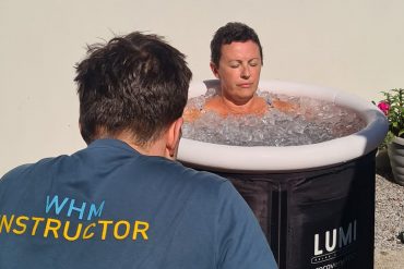 A picture of a woman sat in an ice bath, with a Wim Hof breathing instructor sat in front of her guiding her through the process