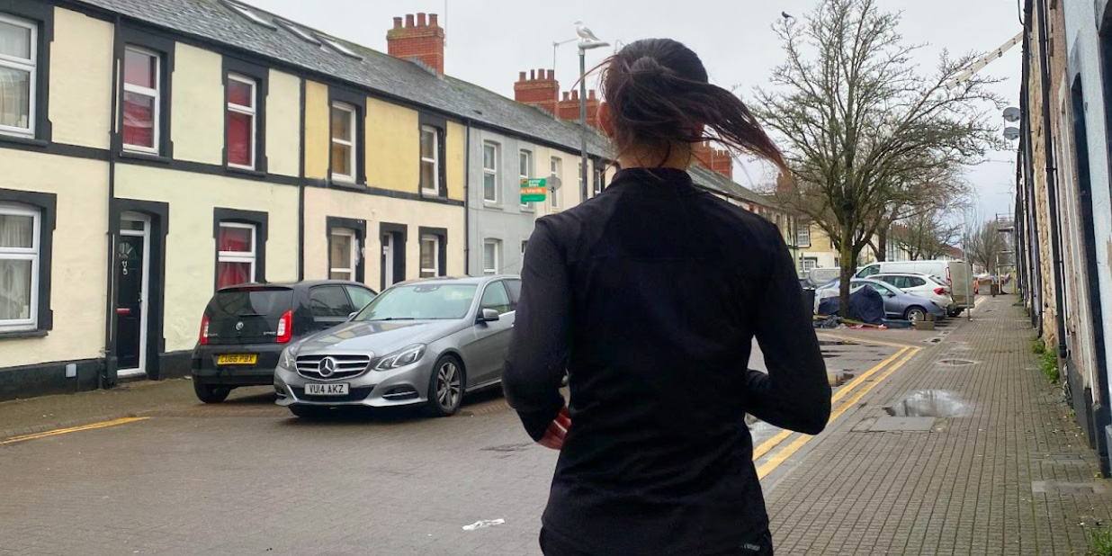 A girl dressed in black running up a street, testing out run recovery methods.