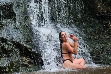 a woman sat on a rock with waterfall falling down on her.