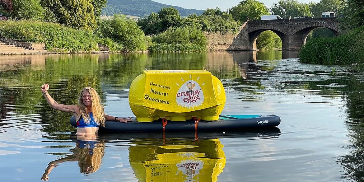 Activist Angela Jones swimming in the River Wye with a box saying 'Crappy Eggs'.