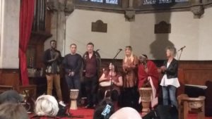 A group of drummers and singers perform in a church hall.