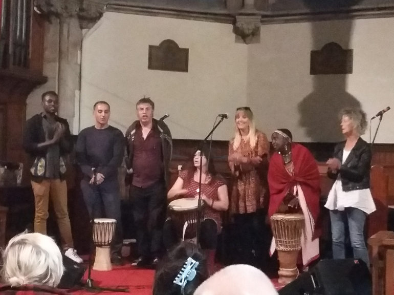 A group of drummers and singers perform in a church hall.