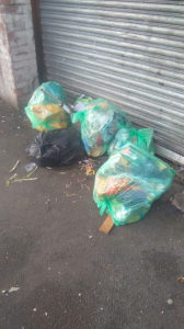 A collection of bin bags sits outside a garage door.