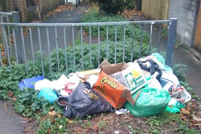 A collection on rubbish bags, boxes, and empty packaging, left near a metal railing in Adamsdown.