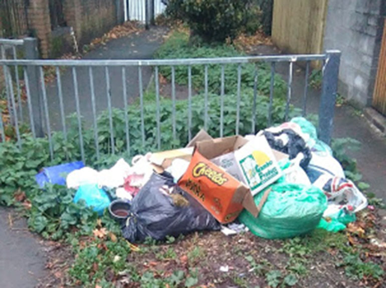 A collection on rubbish bags, boxes, and empty packaging, left near a metal railing in Adamsdown.