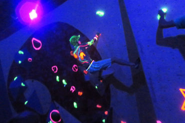 A climber tackles the neon holds in darkness.