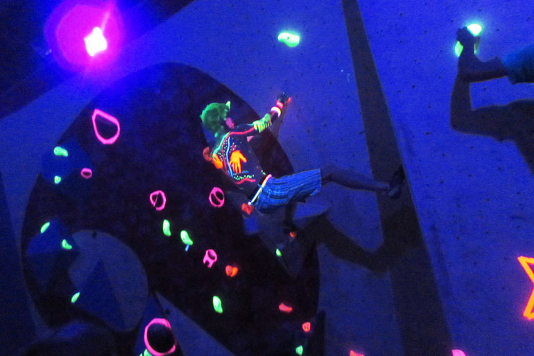 A climber tackles the neon holds in darkness.