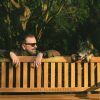 Ricky Gervais poses with a dog behind a bench.