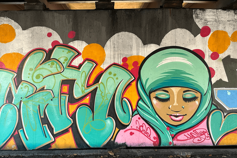 A mural of a girl wearing a hijab with the word 'unity' on a concrete wall