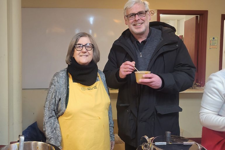 A man and a woman smiling with to vats of soup in front of them