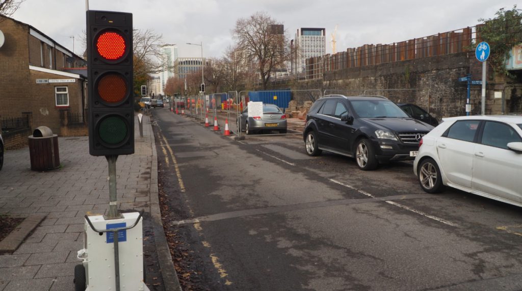 A temporary traffic light on red with a section of road behind it, half of which is closed for the roadwork