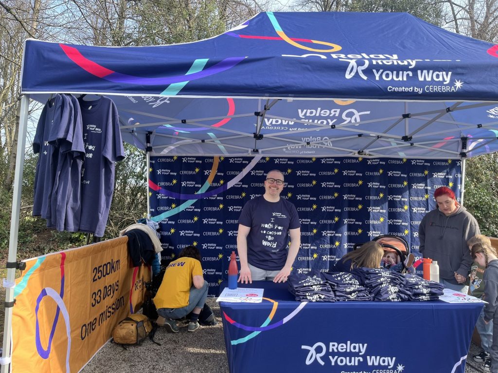 James Hay stood behind a mostly dark blue stall. On the table in front of him are piles of T-shirts made specially for the event. The T-shirts have the text 'I want you to conquer the world' written by a young child.