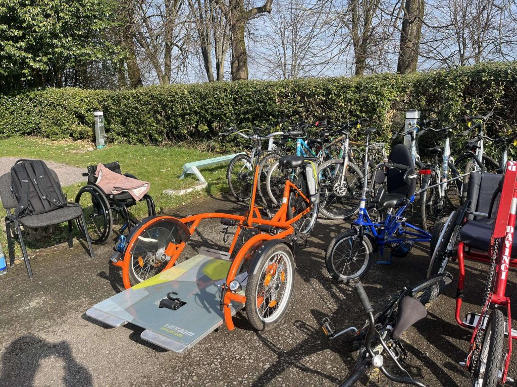 A bright orange trike, which has a space on the front for a wheelchair user.